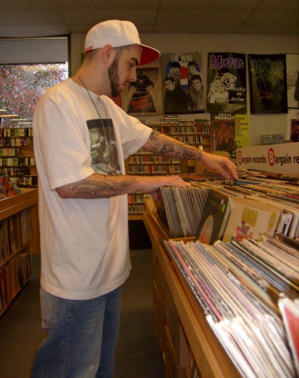 Photo of male wearing baseball hat, baggy shirt and very baggy jeans while looking through music disks.