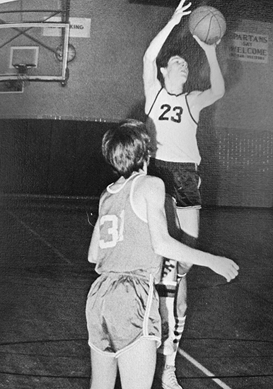 Black and white photograph showing a boy shooting a basket at a school basketball game.