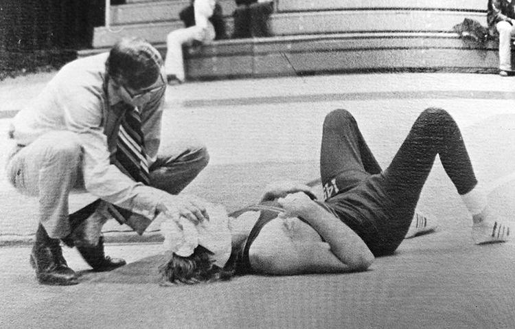Black and white photo of a coach icing the face of an injured West Springfield wrestler on the mat.