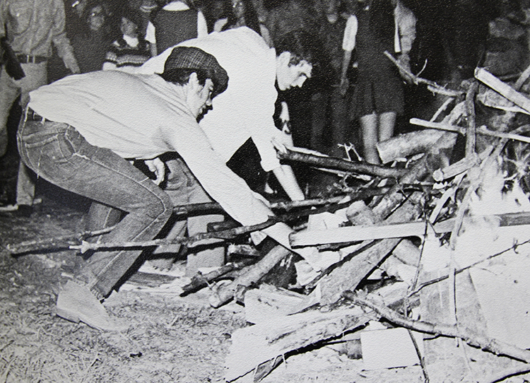 Black and white photograph depicting many male students adding firewood to the annual school bonfire.