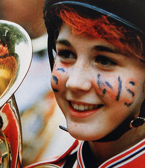 Photograph of girl with a painted face playing in the marching band.